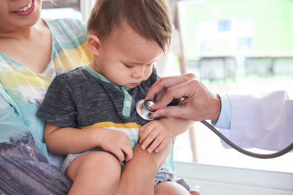 Cute toddler sitting on his mother's knees while doctor listening to his heart beat